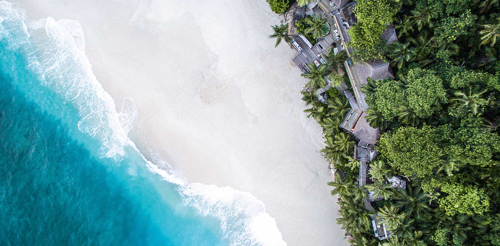 Blick auf ein Luxus-Hotel am Strand, umgeben von Palmen, aus der Vogelperspektive